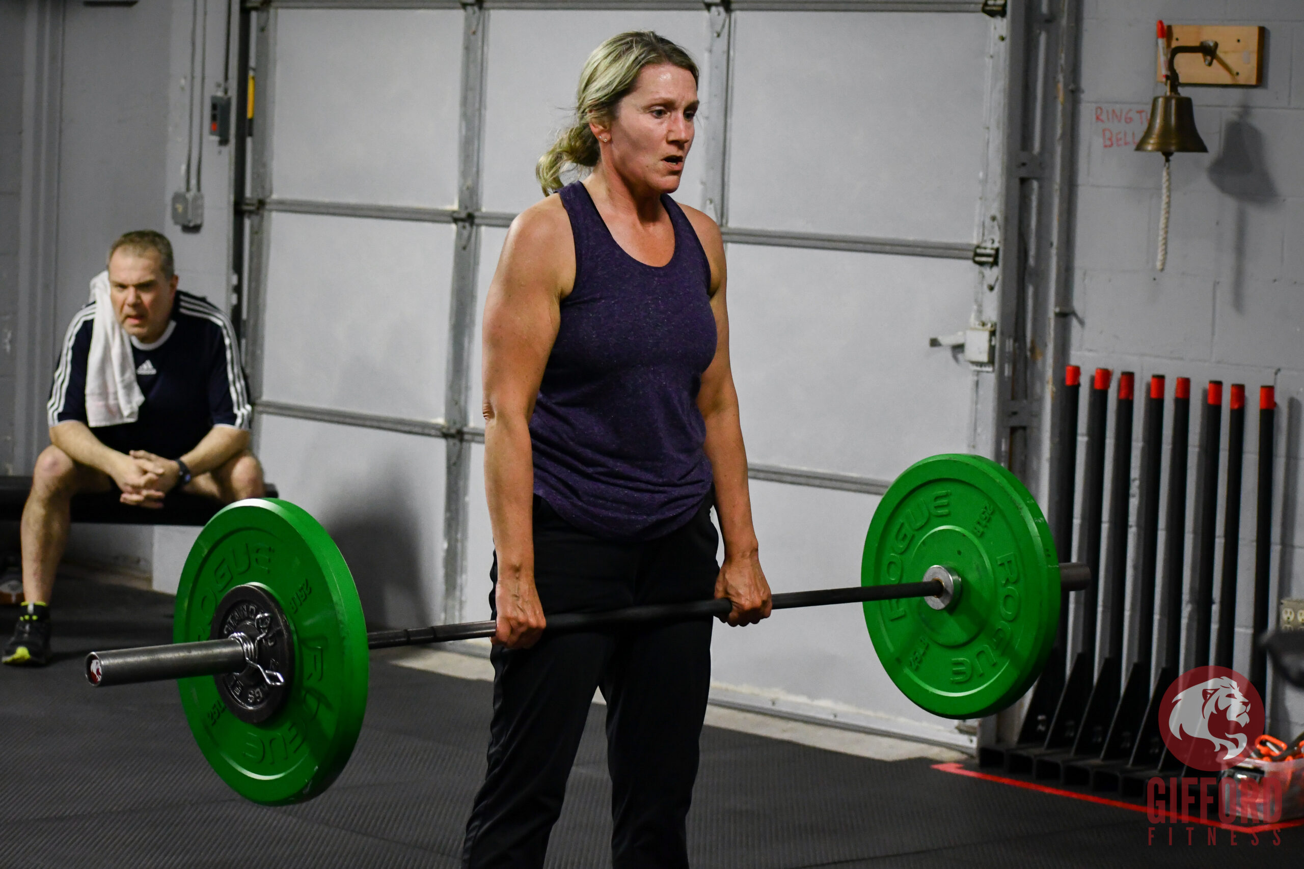 Angie stands at the top of a deadlift with barbell in hand
